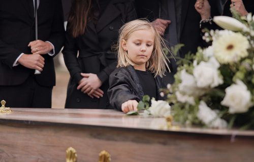Death, grief and girl at funeral with flower on coffin, family and sad child at service in graveyard for respect. Roses, loss and people at wood casket in cemetery with kid crying at grave for burial